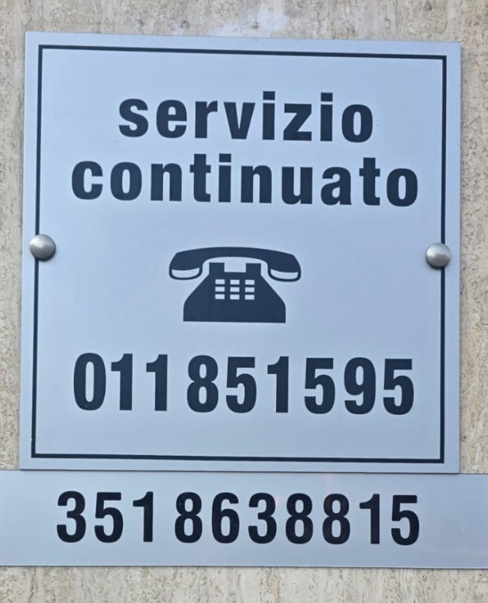 Targa servizio continuato con i numeri 011 851595 e 351 8638815 all'ingresso dell'agenzia